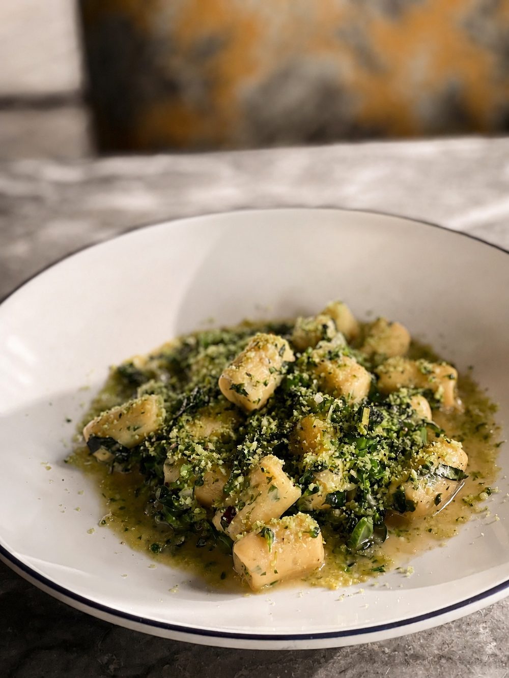 Potato gnocchi with wilted greens and an herb sauce, finished with a green crumb, in a white bowl.