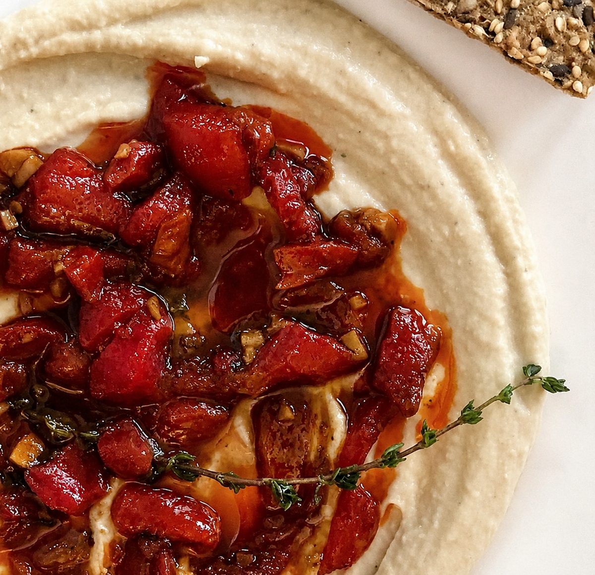 Whipped white bean purée swirled on a plate, topped with roasted red peppers, garlic, olive oil and a sprig of thyme, with a seeded cracker.
