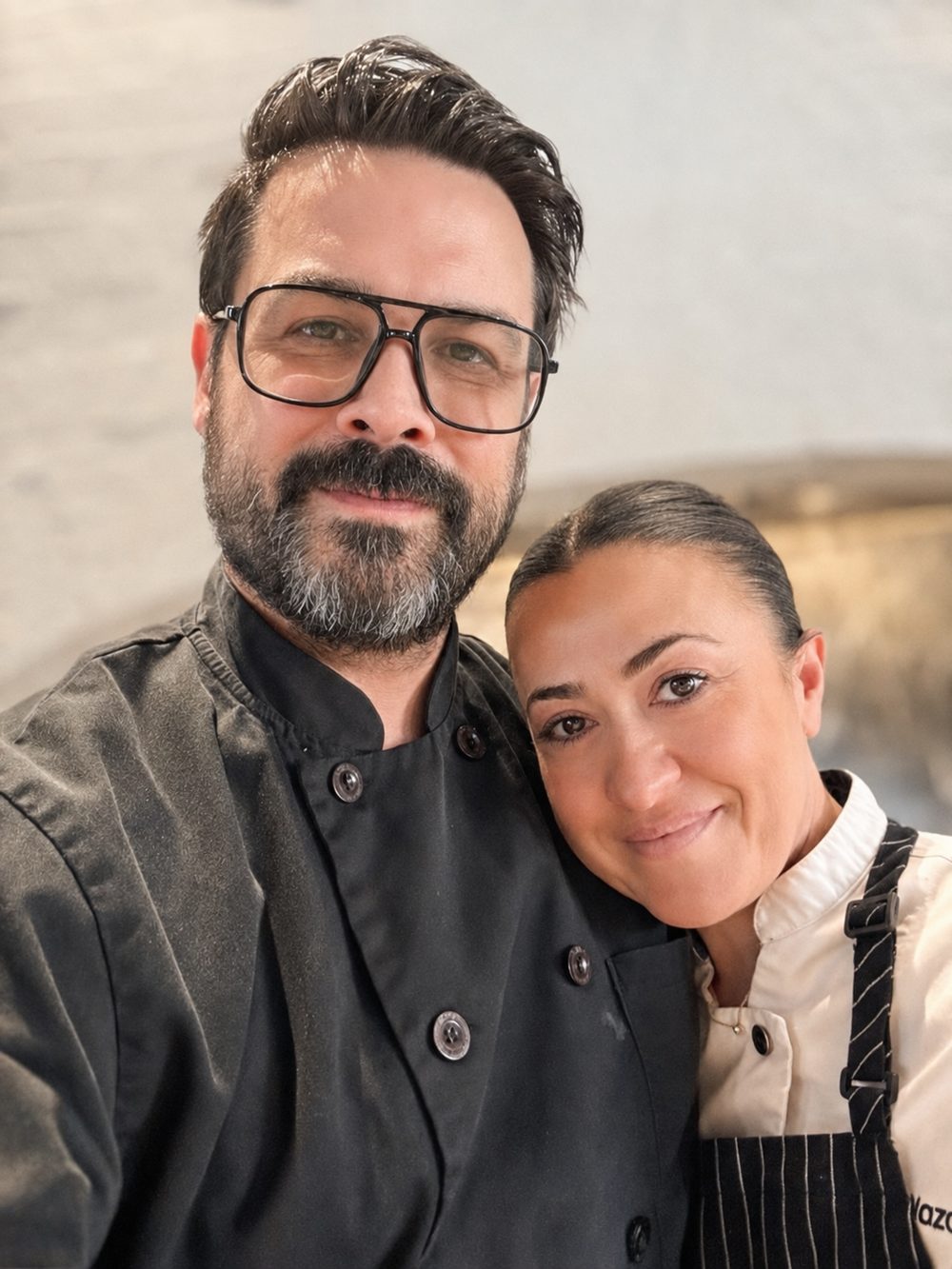 Jesse Brune and Chef Manifa Nazarian in chef jackets, heads together, in a kitchen.