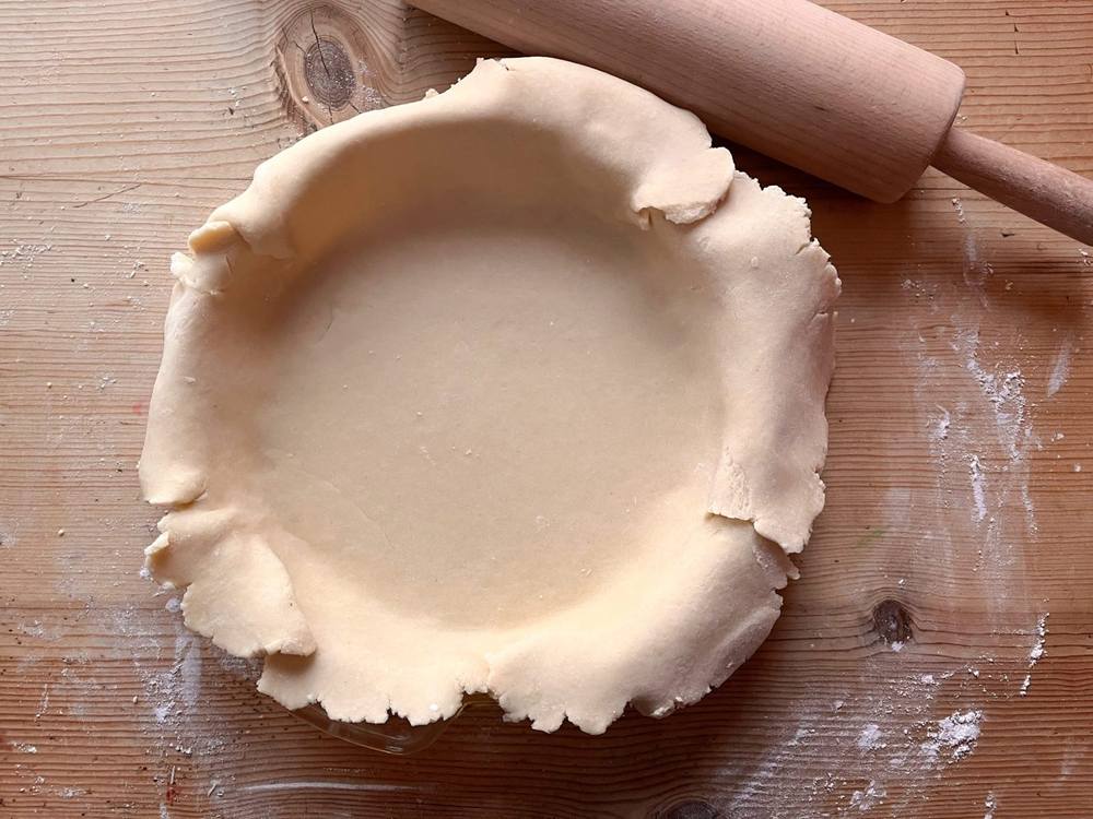A pastry crust pressed into a pie dish on a floured wooden bench, rolling pin alongside.