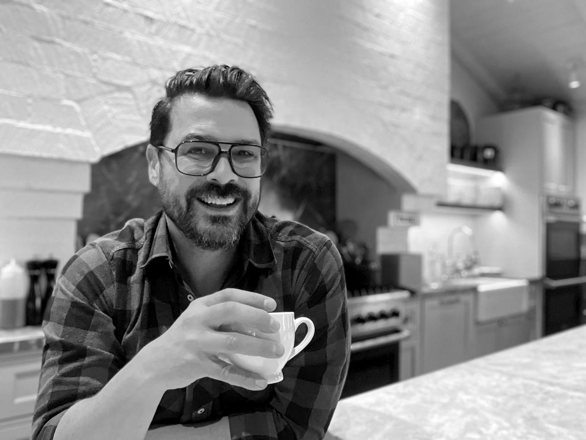 Jesse Brune laughing at the kitchen counter, holding a coffee cup.