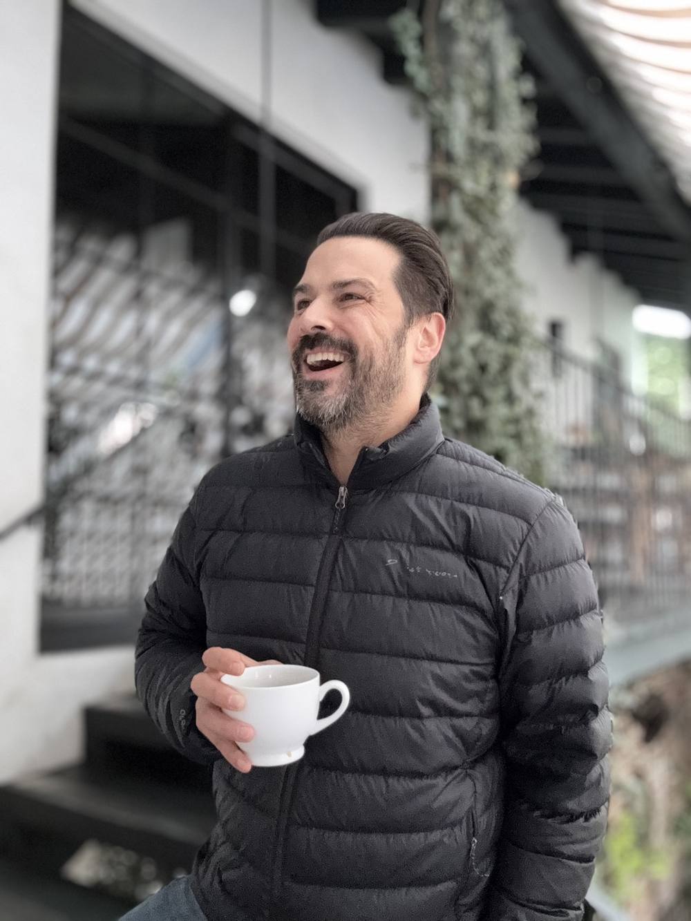 Jesse Brune laughing outside a restaurant, holding a coffee cup.