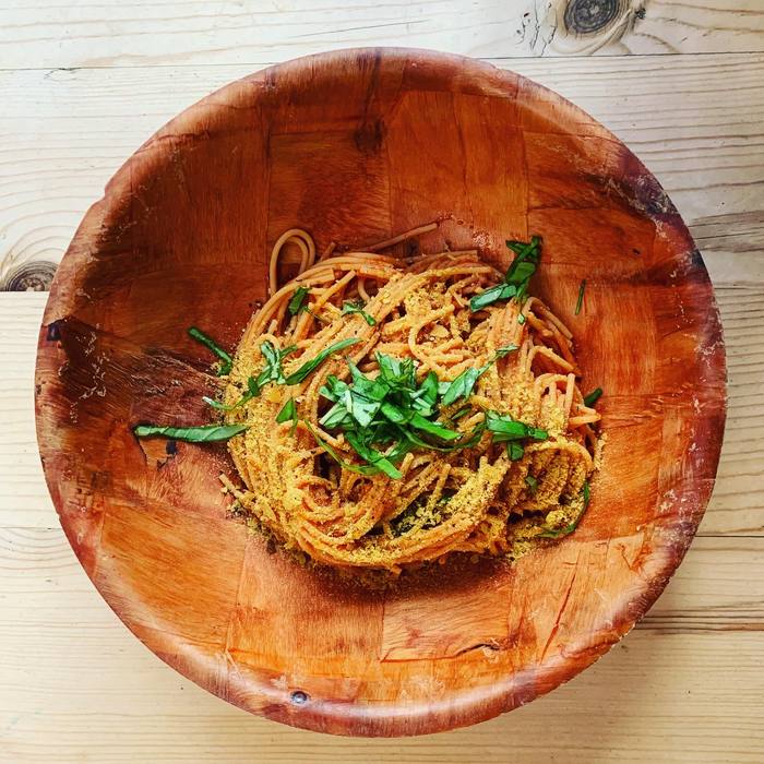 Spaghetti in a wooden bowl with tomato sauce, nutritional yeast and torn basil.